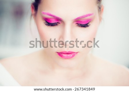 The woman with a bright pink make-up, pink eyebrows and false eyelashes. Studio portrait.