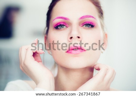 The woman with a bright pink make-up attentively looks forward. Studio portrait.