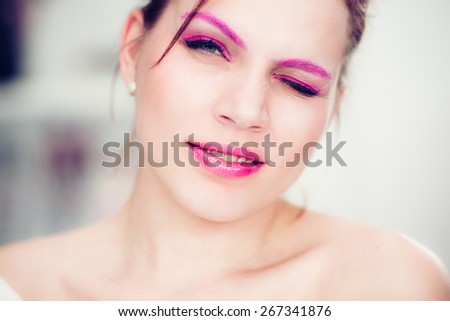 The woman with a bright pink make-up winks. Studio portrait.