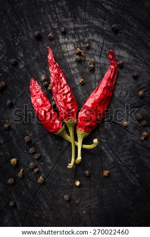 Some hot red peppers and black pepper lie on a dark board