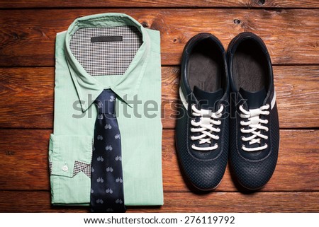 Man\'s collection of clothes in casual style consisting of a men\'s shirt with a tie and footwear on a wooden background