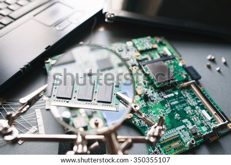 Desktop with broken disassembled laptop. Electronic parts of pc. Analysis computer ram (memory) through magnifying glass.