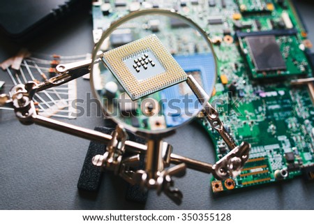 Desktop with broken disassembled laptop. Electronic parts of pc: motherboard, microprocessor. Analysis computer cpu through magnifying glass.