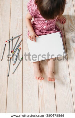 Unrecognizable child learns to draw with colored pencils. Girl sitting on the wooden floor and draw simple drawings.