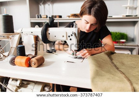 seamstress sews clothes and put thread in needle. Workplace of tailor - sewing machine, rolls of of thread, fabric, scissors.
