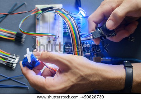 Robotics development closeup., electronic invention. Engineer, programmer, inventor hands with special cables, wires, working with breadboard and constructing robot at home. Modern technologies. Hobby