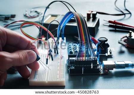 Circuits creation with electronic components. Closeup on programmer hand connecting led with breadboard and microcontroller. Programming, electronics development, innovation in technologies