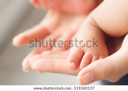 Tiny newborn baby foot in female hands, close-up. Cute little kid leg. Maternity, love, care, new life concept