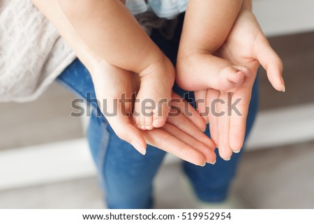 Tiny newborn baby legs on female hands, close-up. Mother holding her kid feet in shape of lovely heart. Love, care, happy family concept