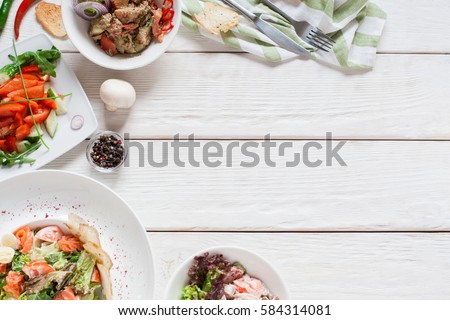 Appetizing meat side dishes frame flat lay. Top view on white wooden table with warm salads. Restaurant menu, buffet, banquet, party concept