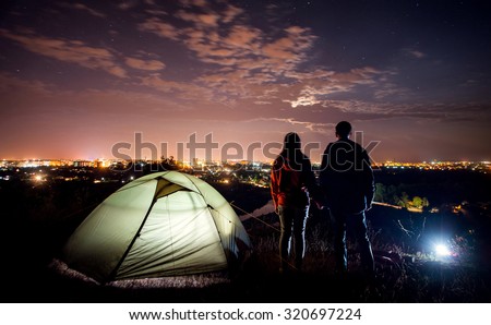 night camping near the town. a young couple holding hands and looking at night city