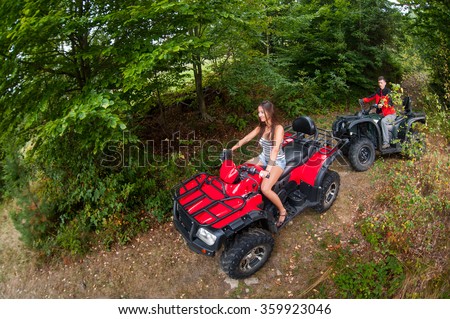 Happy beautiful couple driving four-wheelers ATV. Girl is leading the way