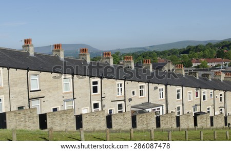A typical row of Lancashire town stone facade built and slate roof covered terraced houses. Red chimney stacks top the buildings with the hills visible in the distance - Taken early morning.