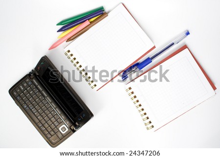 Open palmtop opposite two notebooks with pen and wax pencils