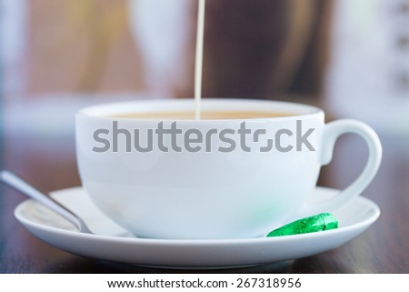 COFFEE AND CREAM.\
Cream is pouring into coffee in a white cup and saucer. shallow depth of field renders the background soft.