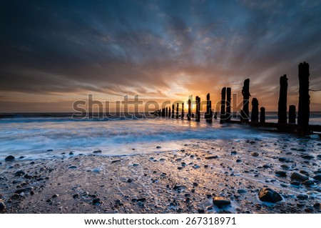 NEW DAWN. A stunning sunrise illuminates the surf and shore whilst silhouetting the remnants of the ancient sea defences.  At Spurn Point, Yorkshire, UK.