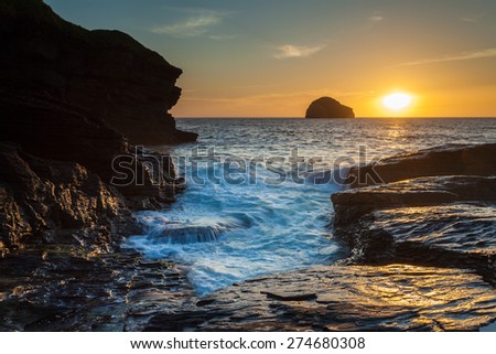 Fools Gold. The warm light of the setting sun turns the rocks to gold as it sinks into the ocean beyond Gull Rock. At Trebarwith Strand, Cornwall, UK.