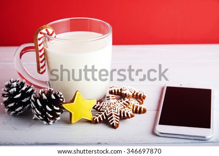 Concept photo: Stay in touch at holidays. Christmas cookies with cup of milk, pine cones and mobile phone at a red background.