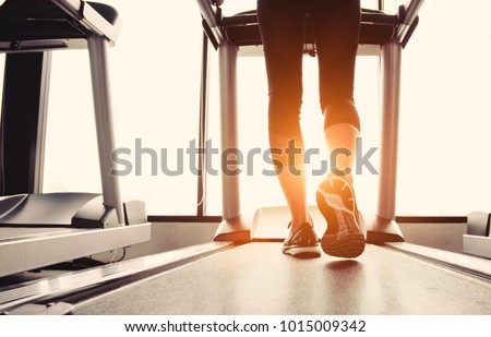 Lower body at legs part of Fitness girl running on running machine or treadmill in fitness gym with sun ray. Warm tone. Healthy and Exercise activity concept. Workout and  Strength training theme.