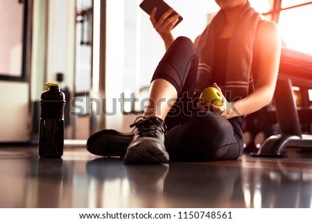 Close up of woman using smart phone and holding apple while workout in fitness gym. Sport and Technology concept. Lifestyles and Healthcare theme.
