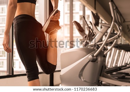 Close up beauty woman stretching legs in workout fitness gym center with sport equipment and treadmill background. Sporty girl warming up before exercise training. Lifestyle and healthy people concept