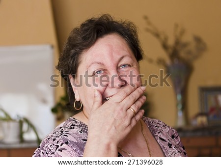 An elderly woman laughs,covering her mouth with her hand