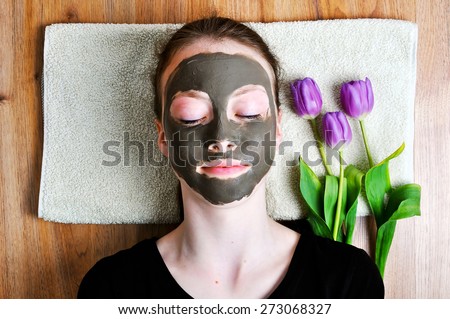 Young woman lying on a towel with a beauty mask and three tulips