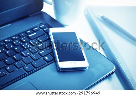 Smartphone put on a laptop with folders and a cup in blue shades