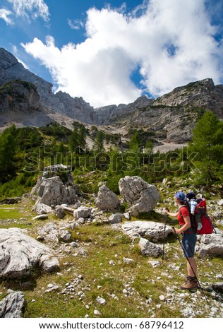 mother with baby carrier carrying a son in alps on a sunny day