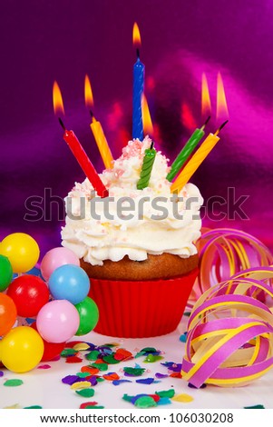 Birthday cupcake with lots of candles, party streamers and colorful confetti over purple background