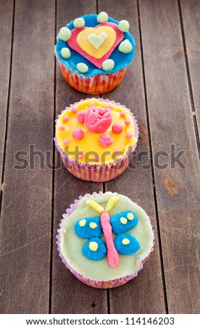three cupcakes with marzipan decoration on wooden background