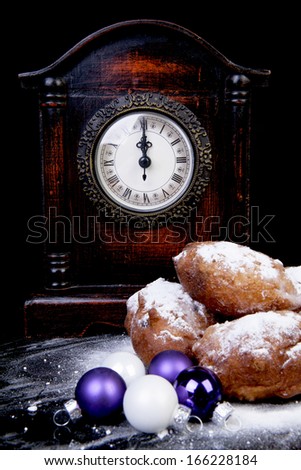 Dutch donut also known as oliebollen, traditional New Year\'s eve food, clock on midnight over black background