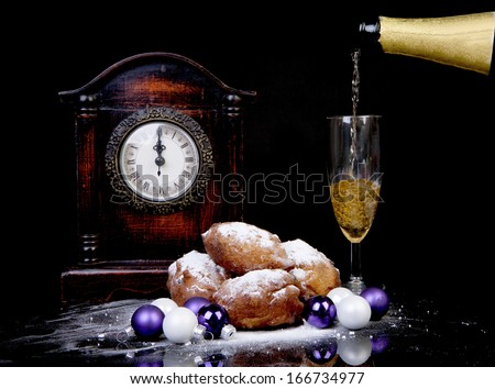 Dutch donut also known as oliebollen, traditional New Year\'s eve food, clock on midnight and champagne over black background