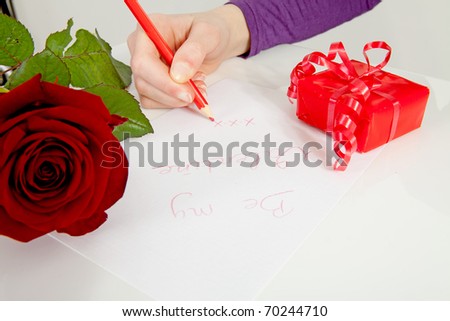 Hand is writing Be my valentine in closeup with rose and present