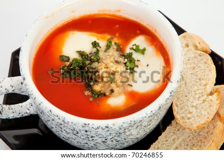 cup with tomato soup and bread in closeup over white background