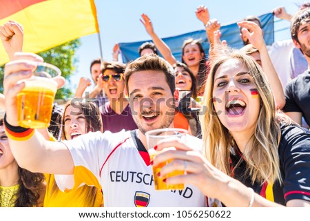 German supporters celebrating at stadium and drinking beer. Group of fans watching a match and cheering team Germany. Sport and lifestyle concepts.