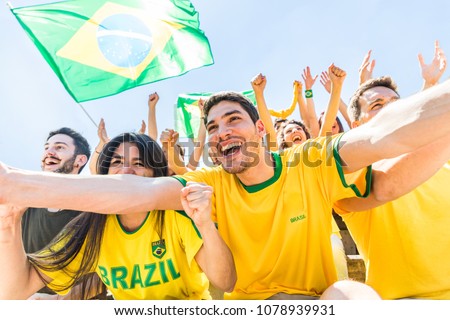 Brazilian supporters celebrating at stadium with flags. Group of fans and friends watching a match and cheering team Brazil. Sport and lifestyle concepts during international cup match
