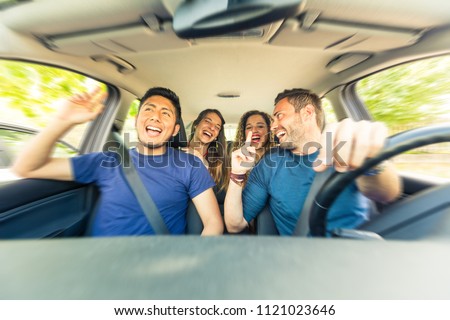 Friends inside the car singing during a road trip . Multicultural group of friends leaving for vacations. Two men sitting on the front and two women on the back singing, laughing and having fun