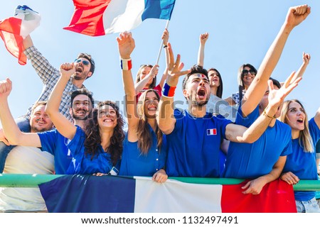 France supporters celebrating at stadium with flags. Group of fans watching a match and cheering team France. Sport and lifestyle concepts.