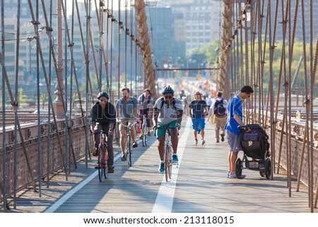 NEW YORK, USA - AUGUST 25, 2014: People cycling and walking on Brooklyn Bridge sidewalk in the morning.