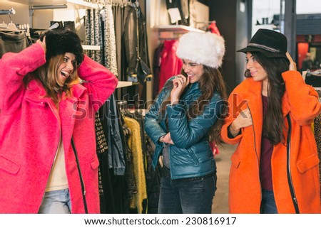 Three Women in a Clothing Store with Colorful Coats. The women are Playing with Strange Clothes and they look each other smiling