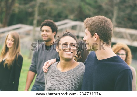 Multiethnic Group of Friends at Park. A caucasian Man with a Mixed-Race Woman are in foreground and some others in background. They seem to be happy