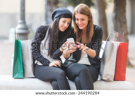Happy Women with Smart Phone and Shopping Bags. They\'re looking at the same Smart Phone looking at Photos or Sending Messages.