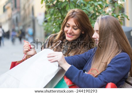 Happy Women with Shopping Bags in the City. Each One Looks in the bag of the other. Friendship and Consumerism themes.