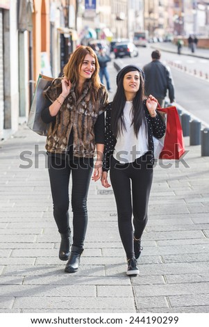 Happy Women Walking in the City with Shopping Bags. They\'re Walking nearby in the Sidewalk and they wear autumn clothes