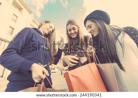 Happy Women with Shopping Bags in the City. Each One Looks in the bag of the other. Friendship and Consumerism themes.