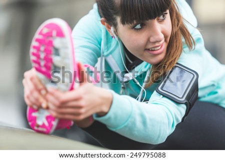 Young Woman Doing Stretching Exercises before Jogging. Focus on the Face. Town Setting in the background.