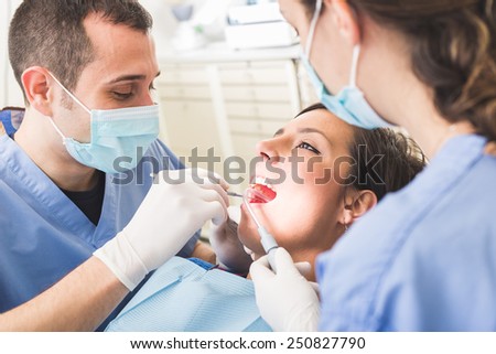 Dentist and Dental Assistant examining Patient teeth. Dentist is a Man, Assistant and Patient are Women. Patient is Smiling and not scared of Dentist.