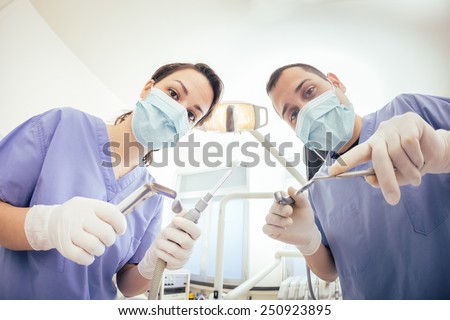 Cheerful Dentists Holding Dental Tools Looking at Camera. Personal or Patient Point of View, POV. They are holding Drill, Mirror, Aspirator and Spreader.