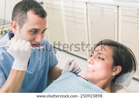 Dentist Scaring Patient with the Drill. Dentist is a Man, Patient is a Woman. Dentist is Holding Drill like a Knife and Patient looks Scared. Funny Representation of Dental Fear.